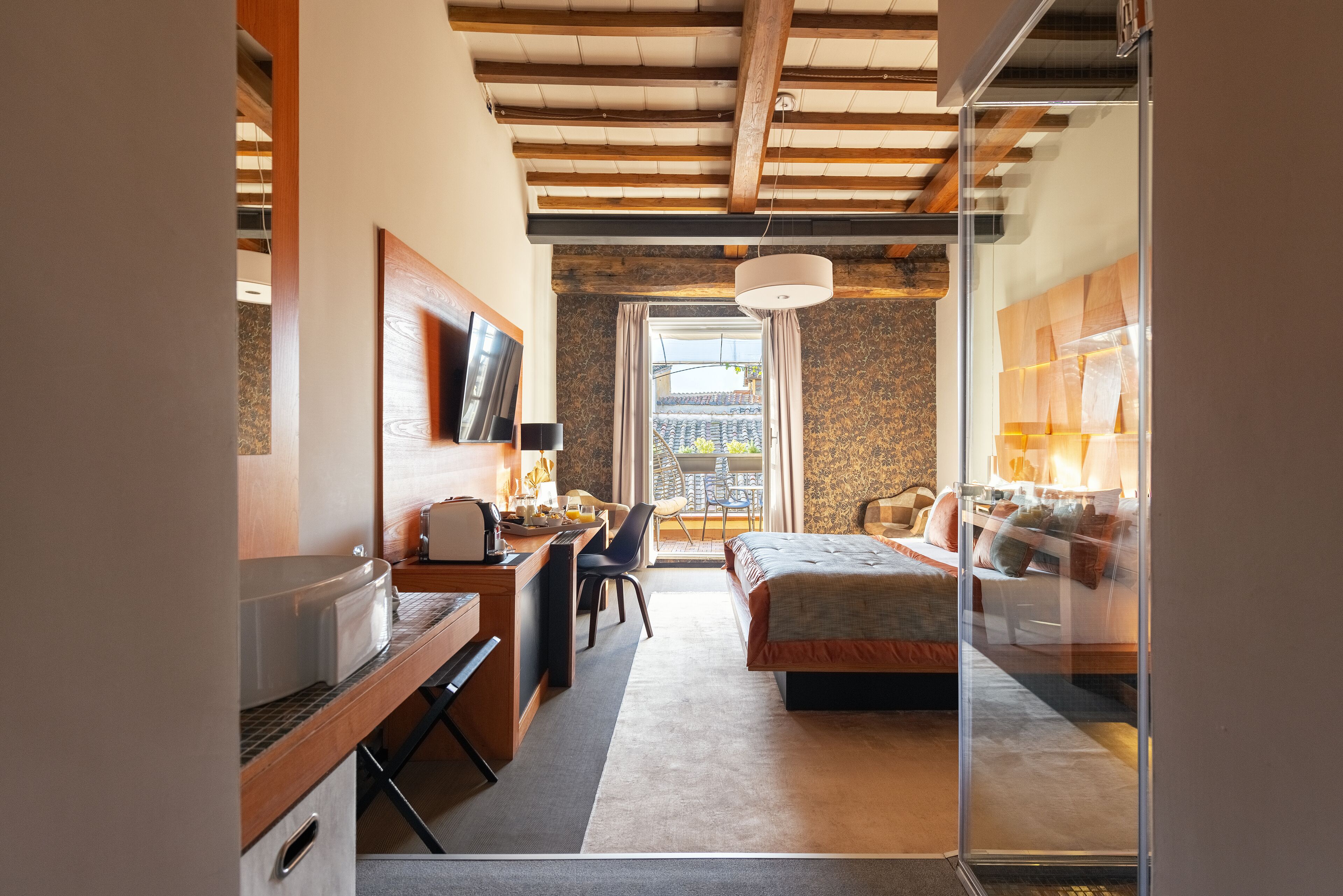 Une chambre d’hôtel moderne avec un plafond en bois, un bureau avec une chaise, un lit et une grande fenêtre avec des rideaux.