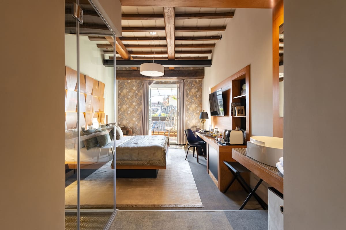 Camera da letto moderna con letto, scrivania e vista sulla città tramite una porta vetrata.