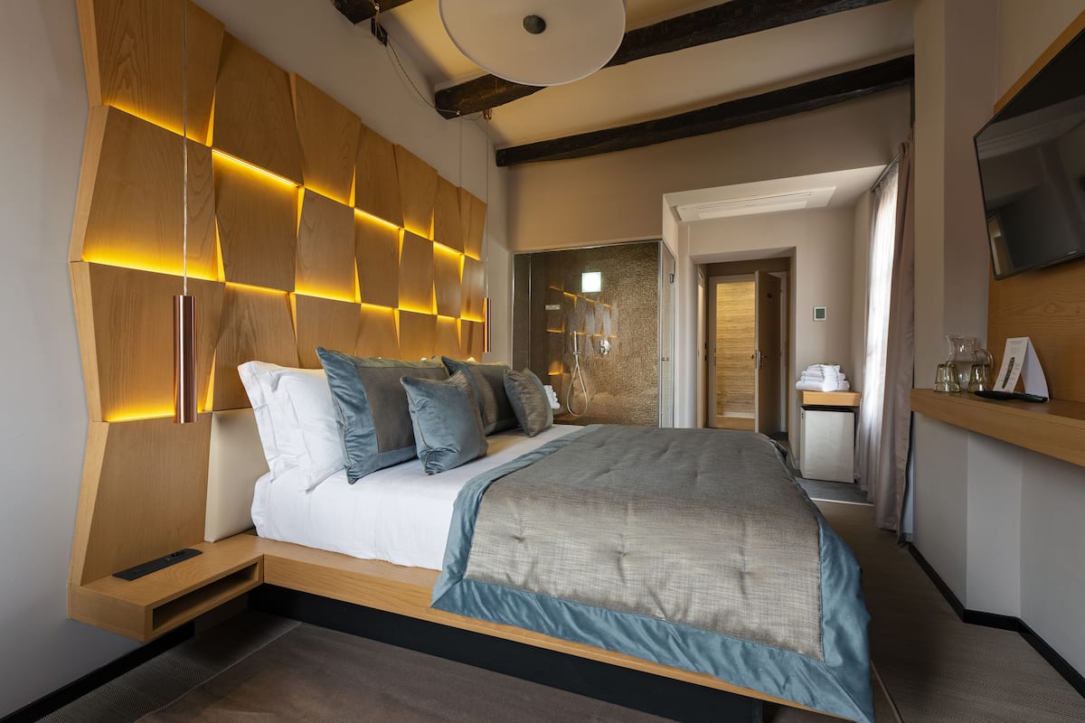 Una camera d'albergo moderna con un letto grande, una testiera in legno e un televisore a schermo piatto.