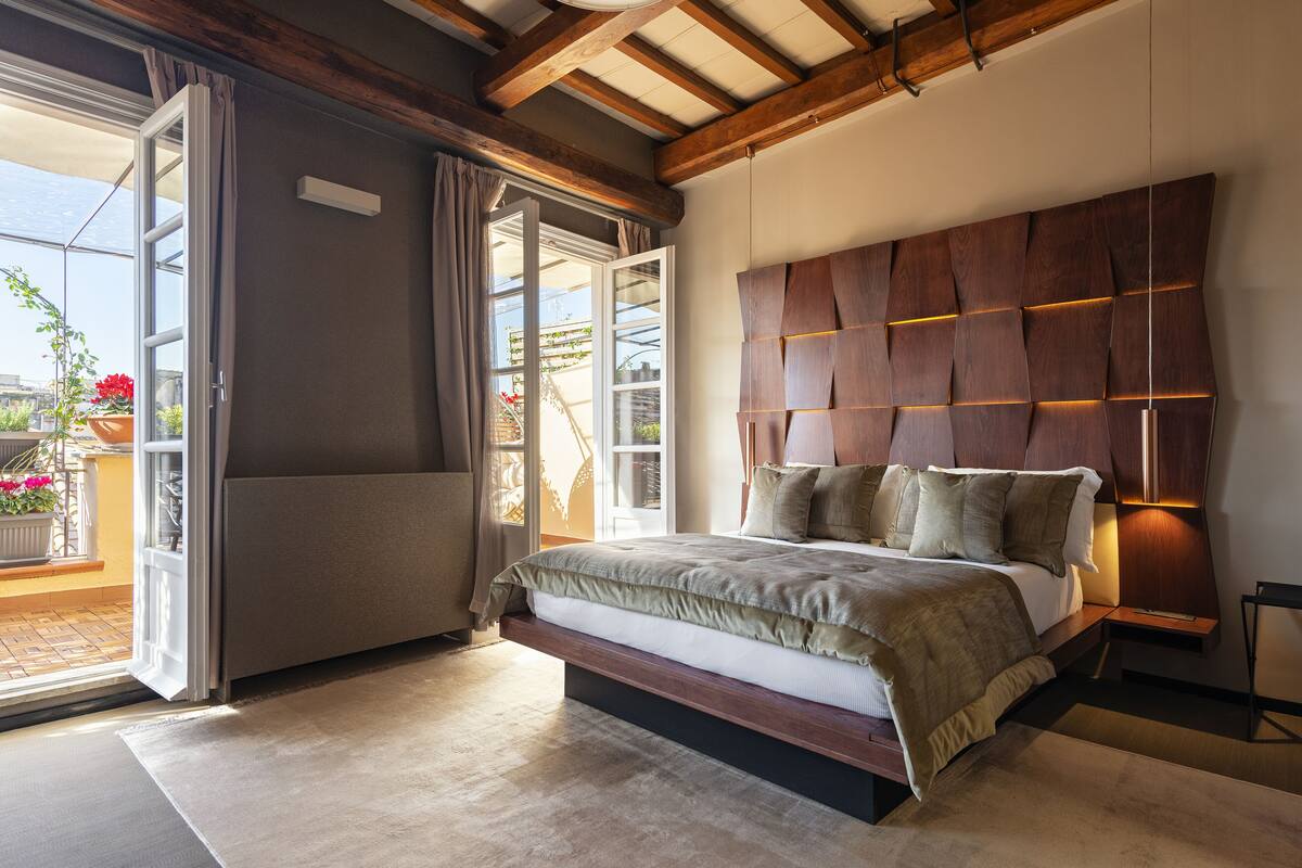 Camera da letto con un letto grande, testiera in legno e una porta a vetri scorrevoli che dà su un balcone.
