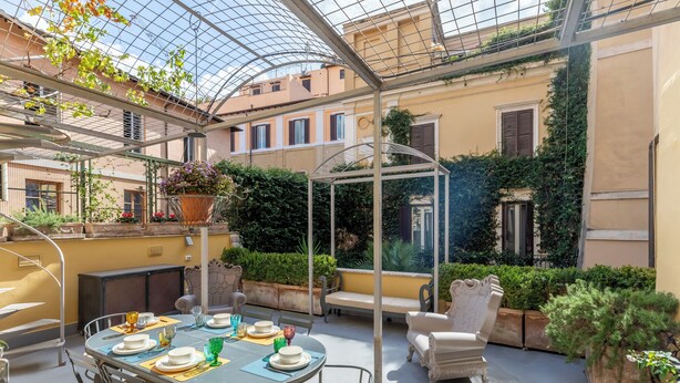 A sunlit outdoor patio with a round table set for dining, surrounded by comfortable seating and potted plants. - Ara di Marte Suites (Rome)