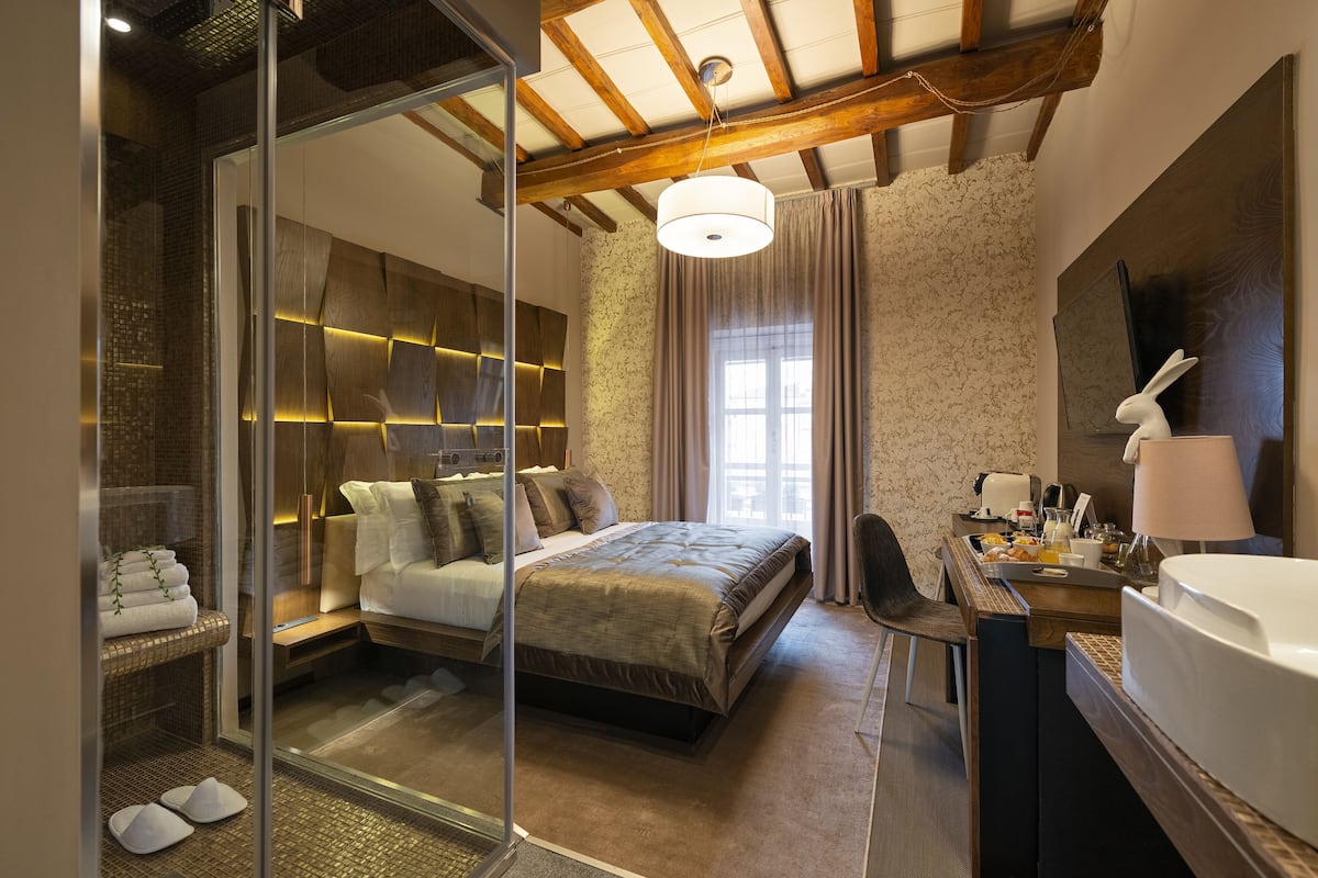 Camera da letto moderna con un letto grande, box doccia in vetro, soffitto in legno e una scrivania con una lampada.