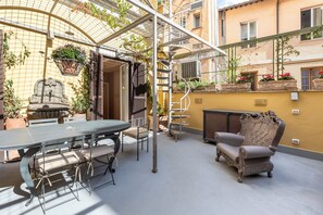A patio with a table and chairs, a decorative chair, a stone fountain, and a metal staircase. - Ara di Marte Suites (Rome)