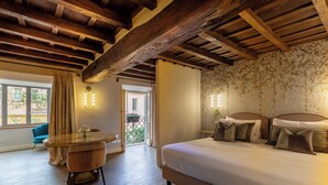 A bedroom with a large bed, wooden ceiling beams, a dining table with chairs, and a view of the outside. - Ara di Marte Suites (Rome)