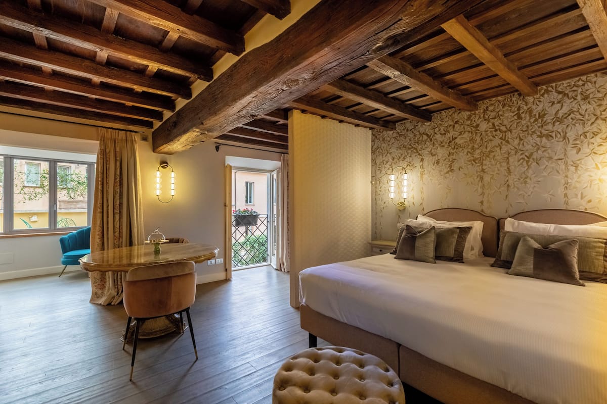 Camera da letto con un letto grande, travi di legno a soffitto, un tavolo da pranzo con sedie e vista sull'esterno.
