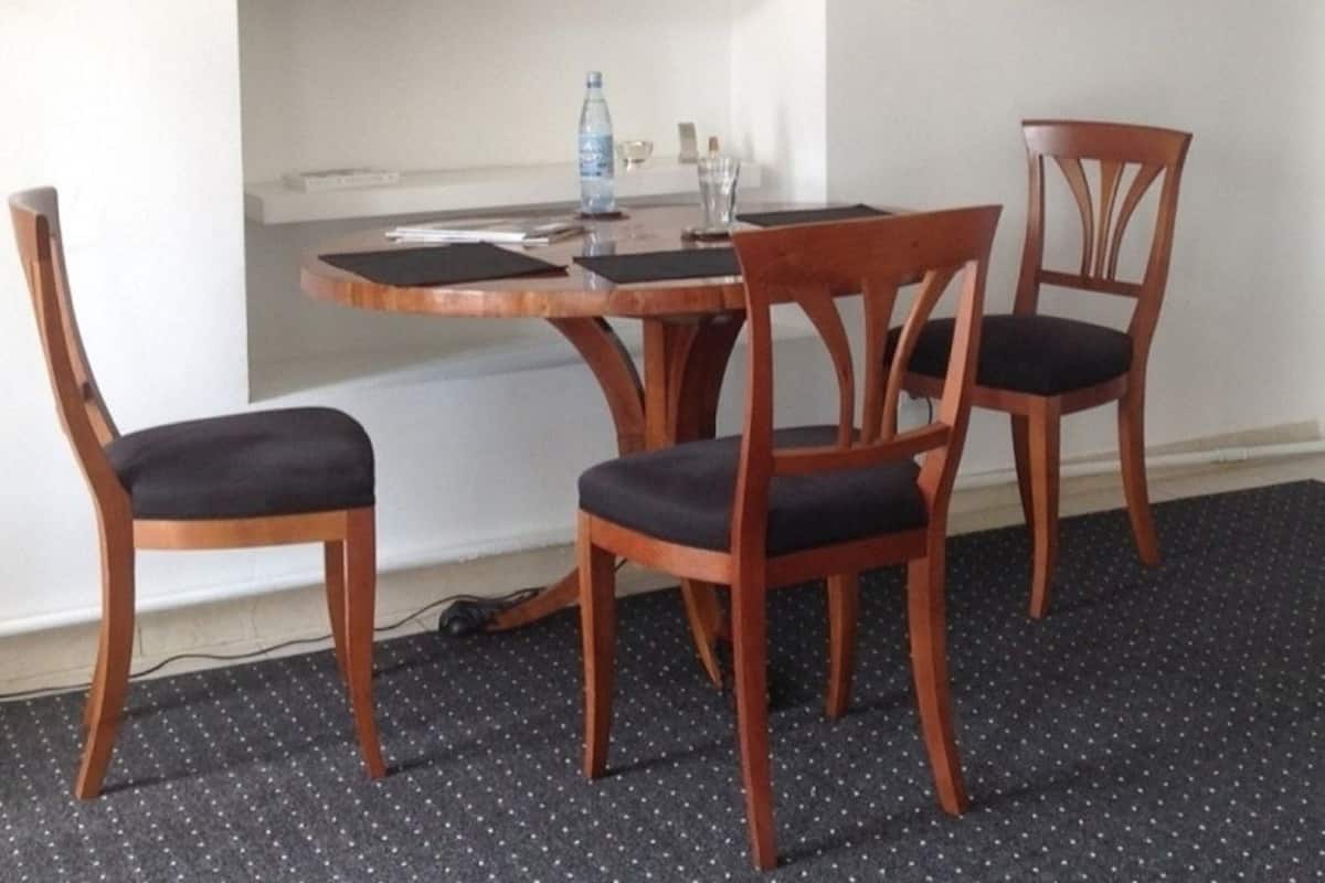 Un comedor con una mesa redonda de madera, cuatro sillas de madera con asientos acolchados, una botella de agua y un cuadro en la pared.