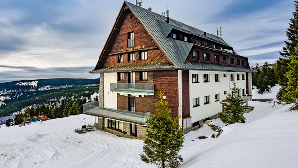 Un edificio de dos pisos con fachada de madera y techo metálico, rodeado de terreno y árboles cubiertos de nieve.