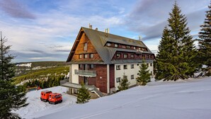 Un gran chalet de varios pisos con techo inclinado, rodeado de nieve y árboles.