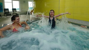 Zona de piscina con dos personas disfrutando del agua, una silla y vistas al exterior.