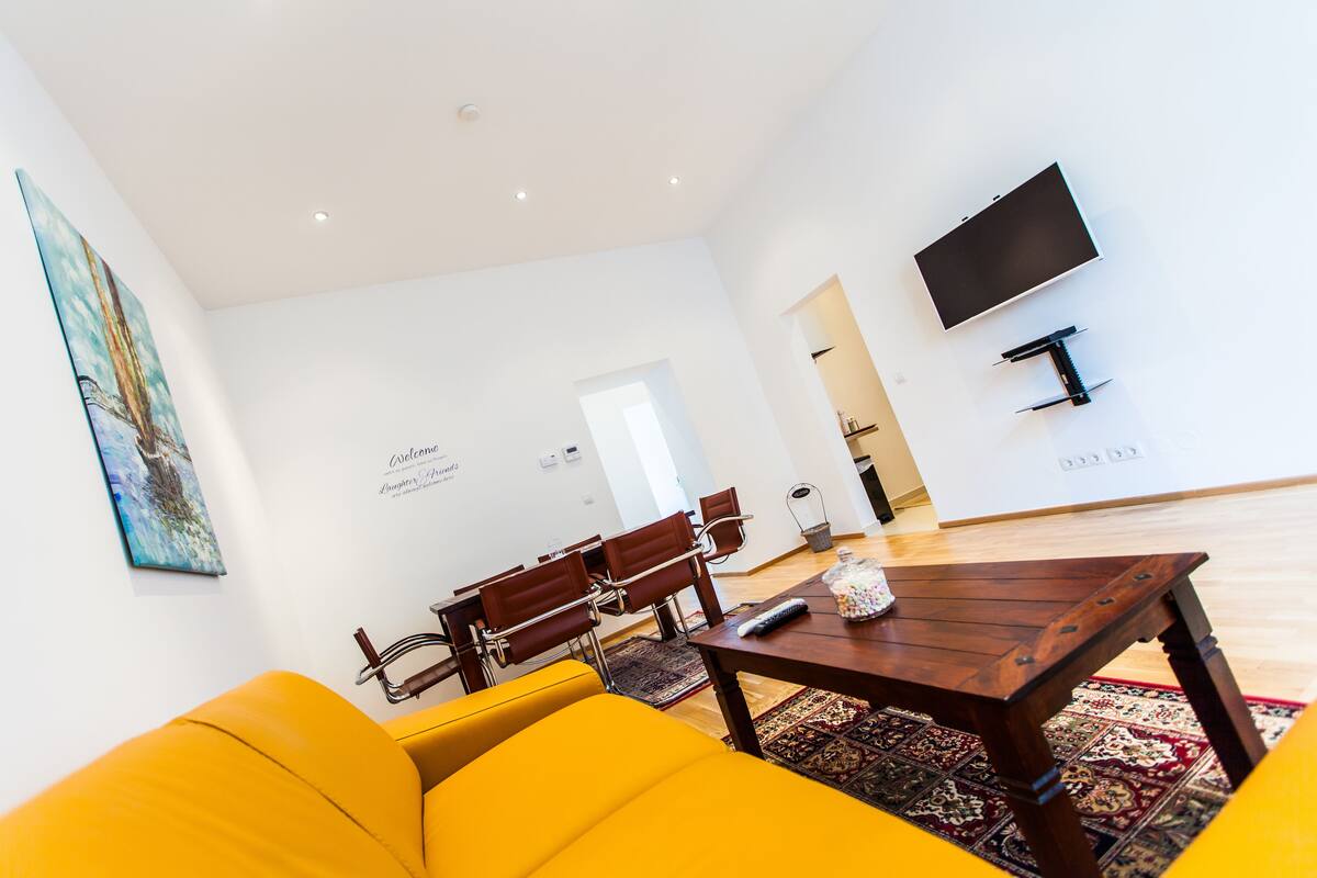 A modern living room with a yellow sofa, wooden coffee table, and a flat-screen TV mounted on the wall.