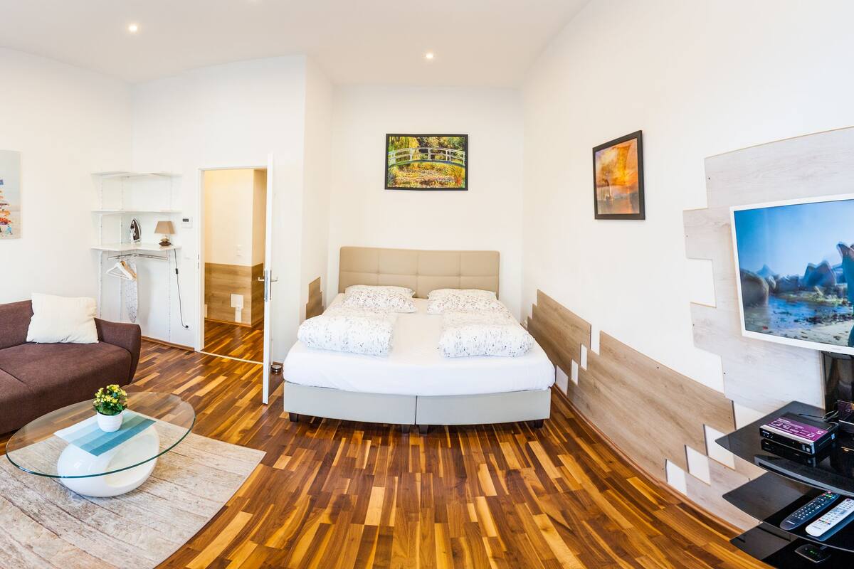 A modern hotel room with a round bed, a sofa, a TV, and a fan.