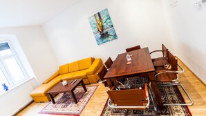 Una sala de estar moderna con un sofá amarillo, una mesa de comedor de madera y sillas, un cuadro en la pared y un ventanal grande.