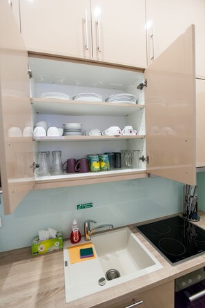 A kitchen with a sink, stove, and cabinets containing dishes and glassware. - Vienna Market Apartment (Vienna)