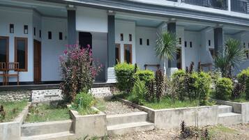 A two-story building with a covered porch, stone steps, and a garden with various plants and shrubs.
