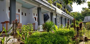 Un edificio con porche cubierto, columnas y jardín con diversas plantas.