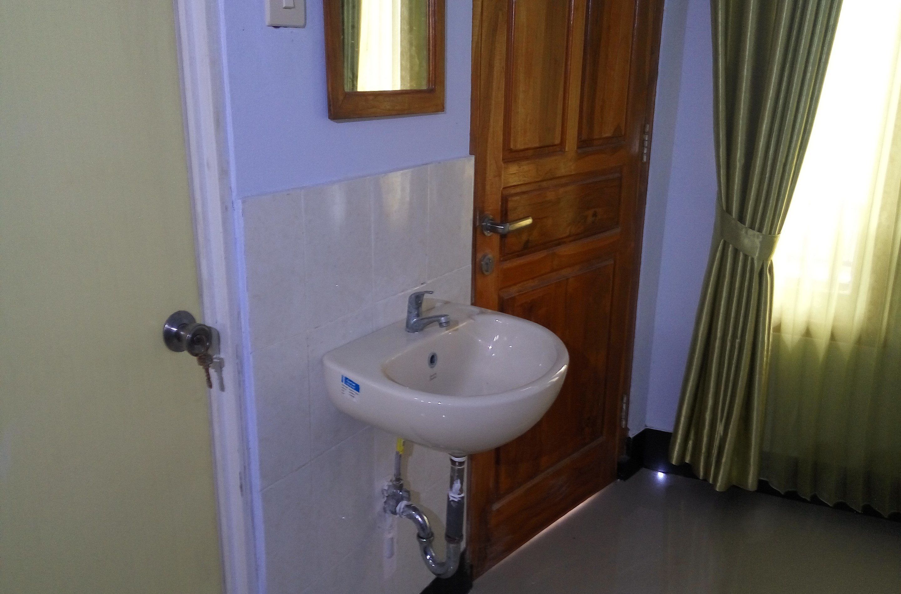 Un baño con un lavamanos blanco, una puerta de madera y un espejo sobre el lavamanos.