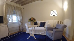 A cozy living room with a white sofa, a grey armchair, a small white table with a vase of flowers, a floor lamp, and a television on a stand. - Palazzo della Stufa - Residenza d'Epoca (Florence)