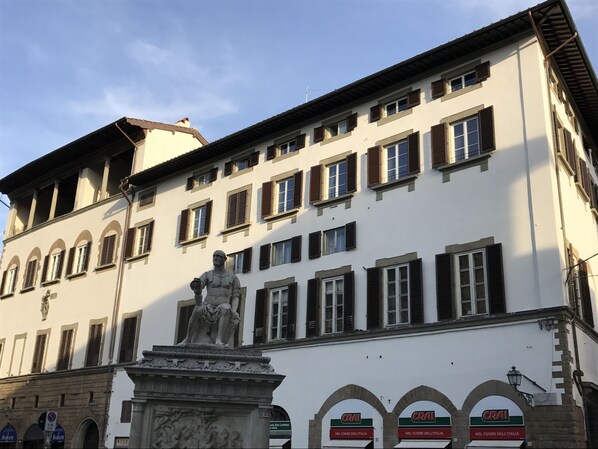Un bâtiment avec une statue devant, de nombreuses fenêtres avec des volets et des enseignes indiquant les magasins « Crai ».