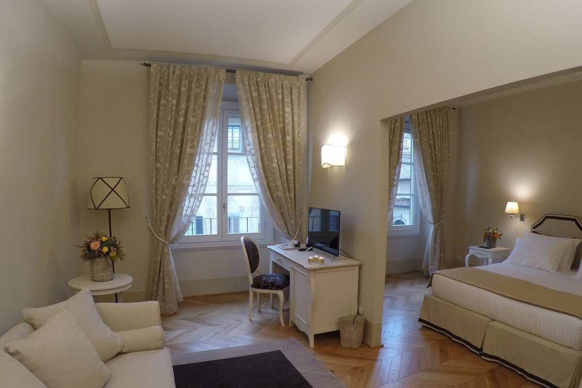 Une chambre d’hôtel comprenant un lit, un bureau avec un ordinateur, une chaise, une petite table avec une lampe et une fenêtre avec des rideaux.