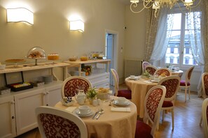 Un espace repas avec des tables rondes, des chaises et un buffet proposant divers plats.