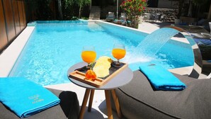 A poolside setting with a table, two glasses of orange juice, a towel, and a water feature. - Hotel Alkima (Kotor)