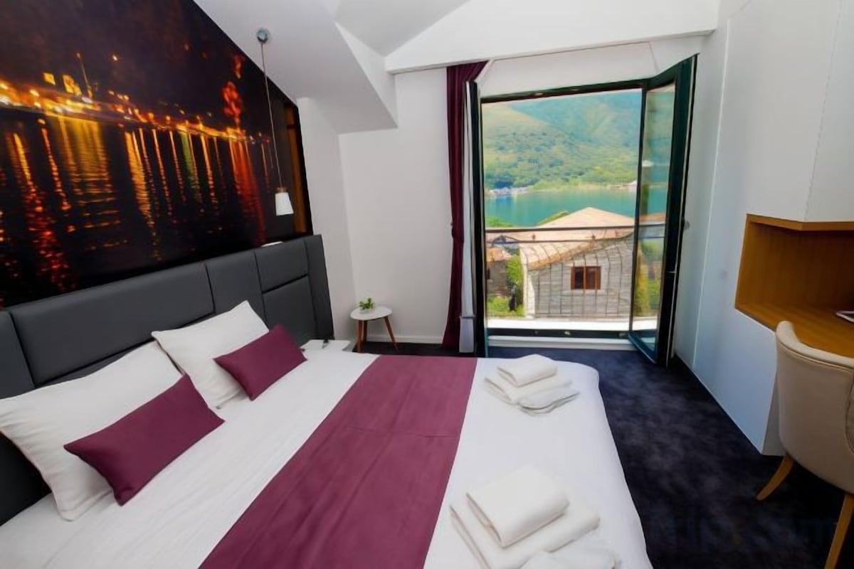 A hotel room with a large bed, a view of a body of water, and a balcony.