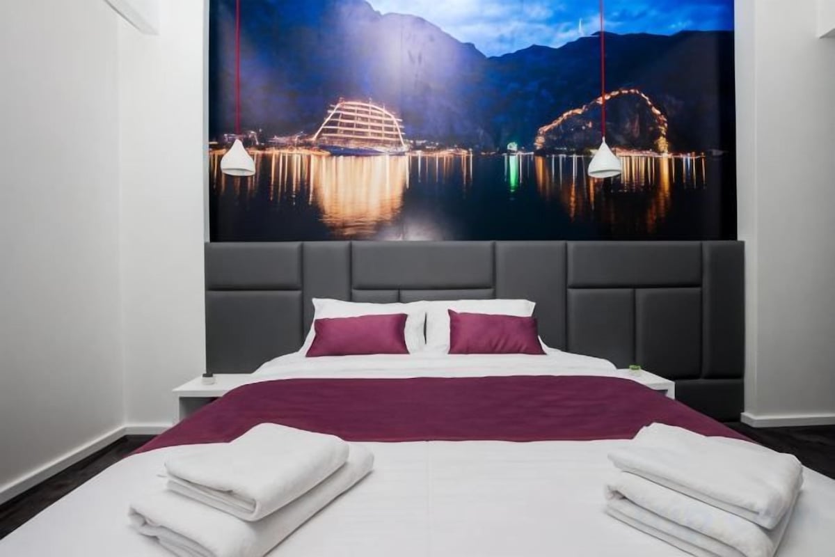 A hotel room with a bed, a large window, and a night view of a cityscape.