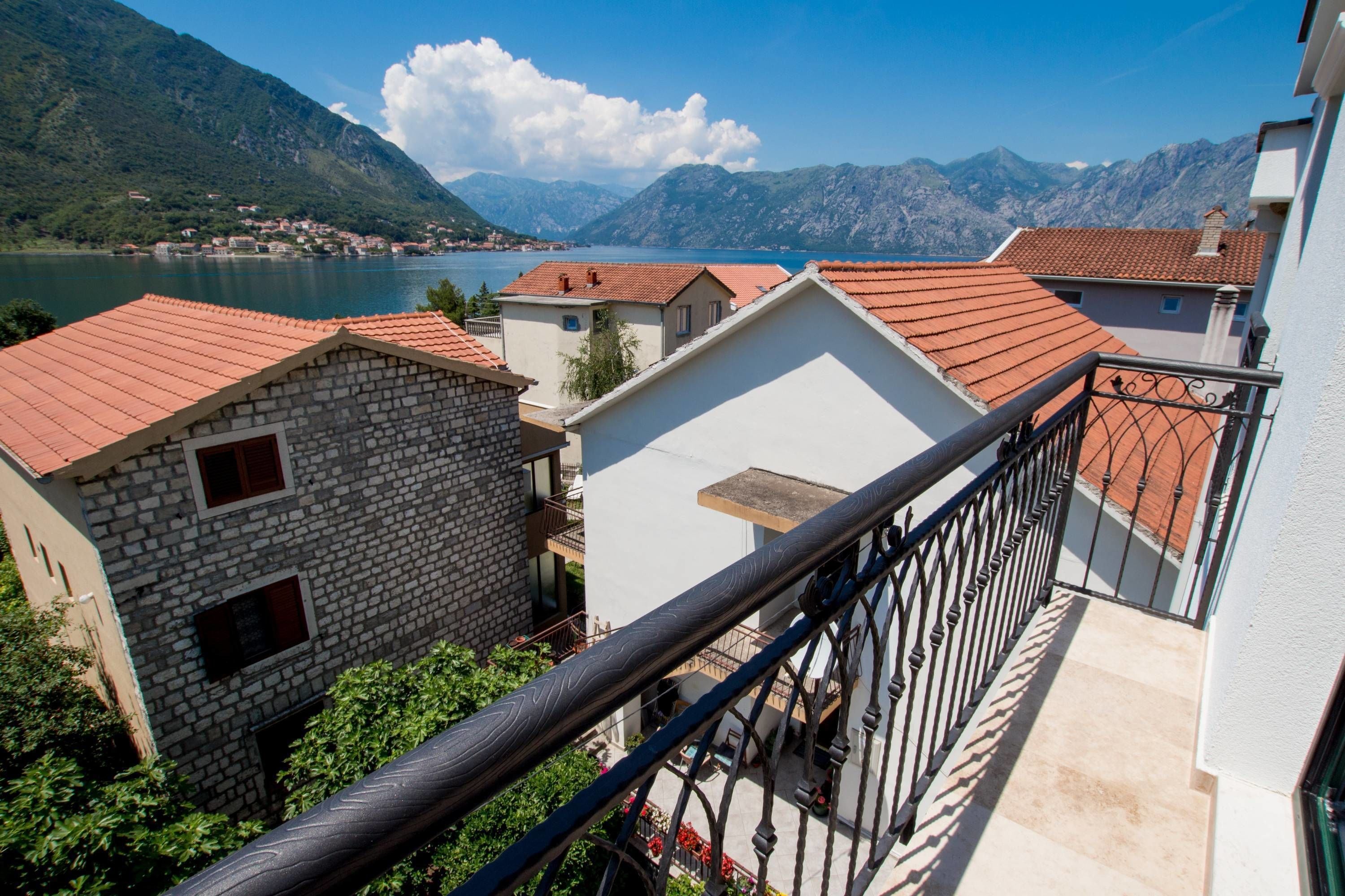 Un barrio residencial con casas adosadas, un balcón con barandilla metálica y un lago con montañas al fondo.