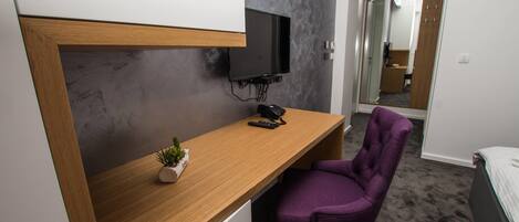 A small room with a desk, a chair, a television mounted on the wall, and a bed.