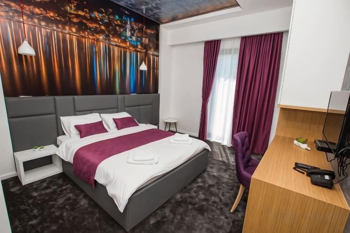 A modern hotel room with a large bed, a desk, and a television.