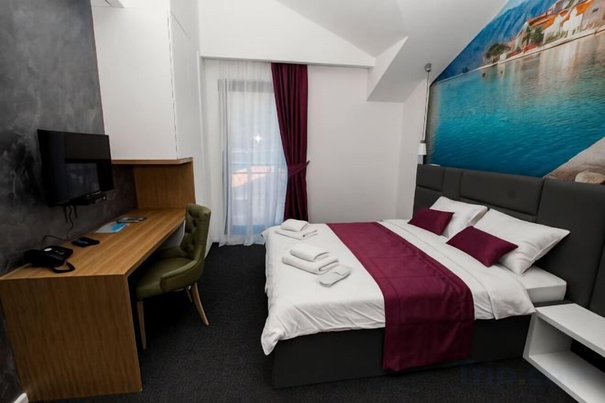 A hotel room with a bed, a desk, a chair, a television, and a window with curtains.