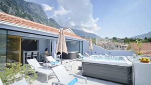 A rooftop terrace with lounge chairs, a hot tub, and a view of mountains. - Hotel Alkima (Kotor)