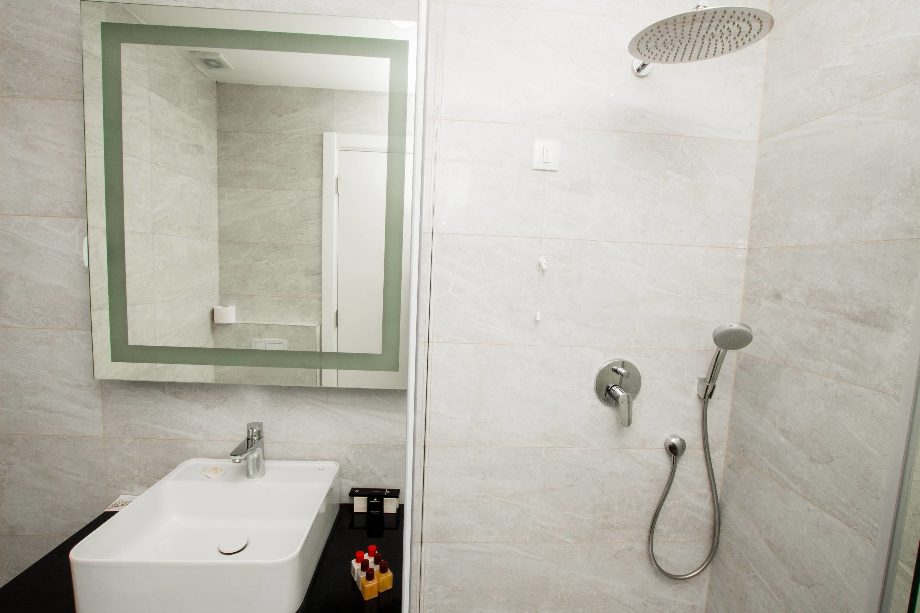 A modern bathroom with a white sink, a mirror, a shower with a handheld showerhead, and a glass-enclosed shower stall.
