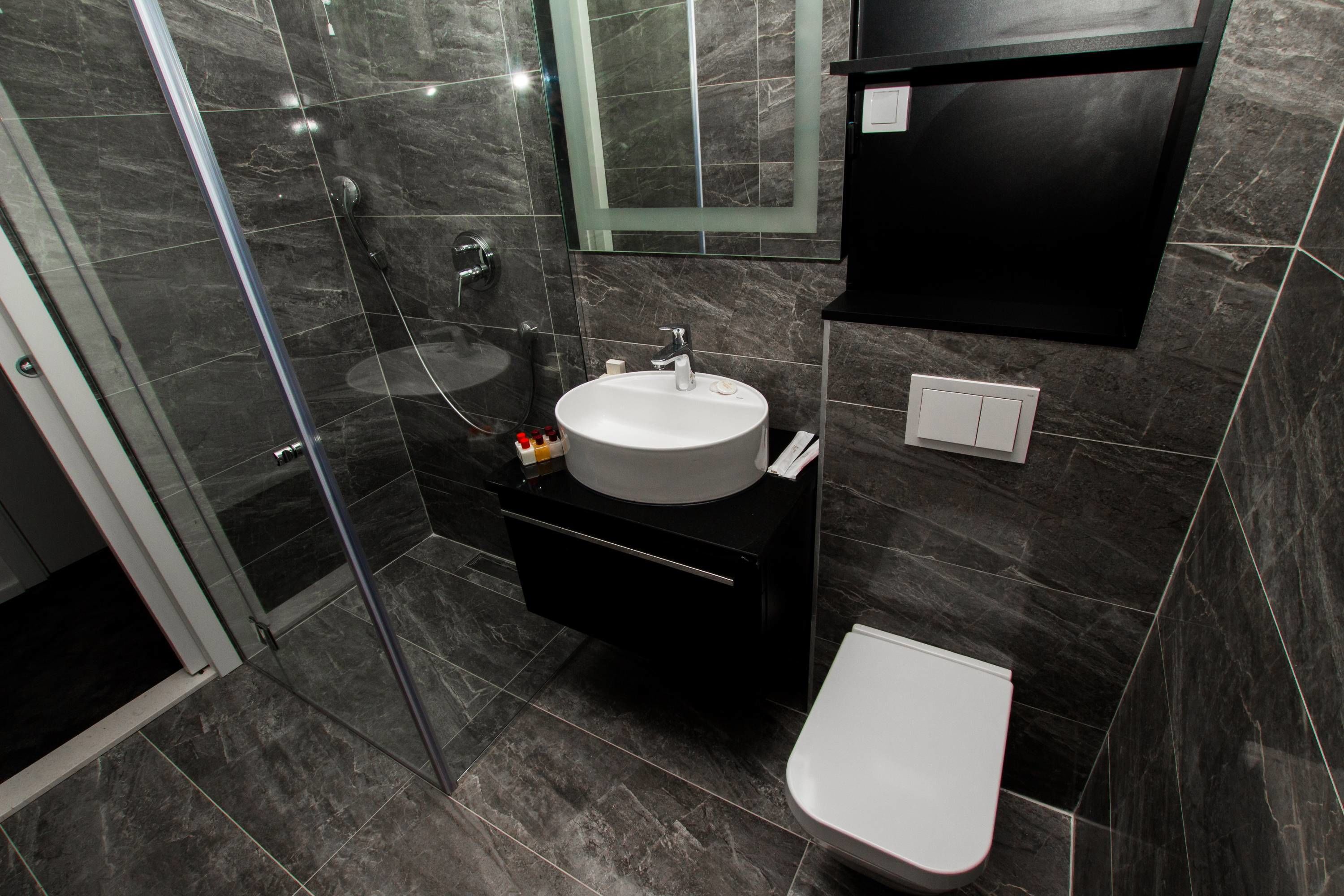 A modern bathroom with a glass shower enclosure, a white sink, and a black vanity.
