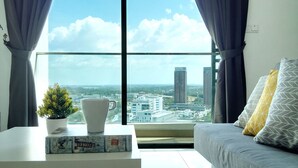 A modern living room with a city view, a white coffee table with decorative items, a grey sofa with patterned cushions, and a potted plant. - Cyberjaya Cybersquare Soho Suites (Cyberjaya)