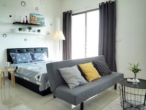 A modern bedroom with a bed, a grey sofa, a small round table, and a painting on the wall.