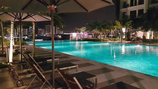 A nighttime pool area with lounge chairs and umbrellas, surrounded by palm trees and a cityscape in the background. - Cyberjaya Cybersquare Soho Suites (Cyberjaya)