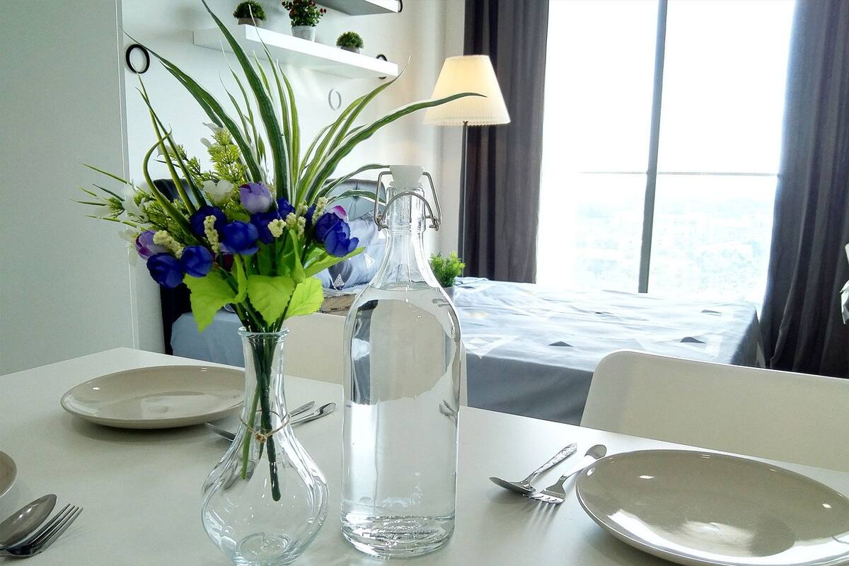 A dining table set with plates, cutlery, a vase with flowers, and a water bottle.