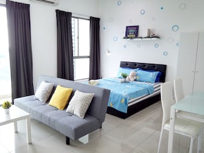 Quarto moderno com sofá cinzento, cama com roupa de cama azul, cadeira branca e uma pequena estante com objetos decorativos.