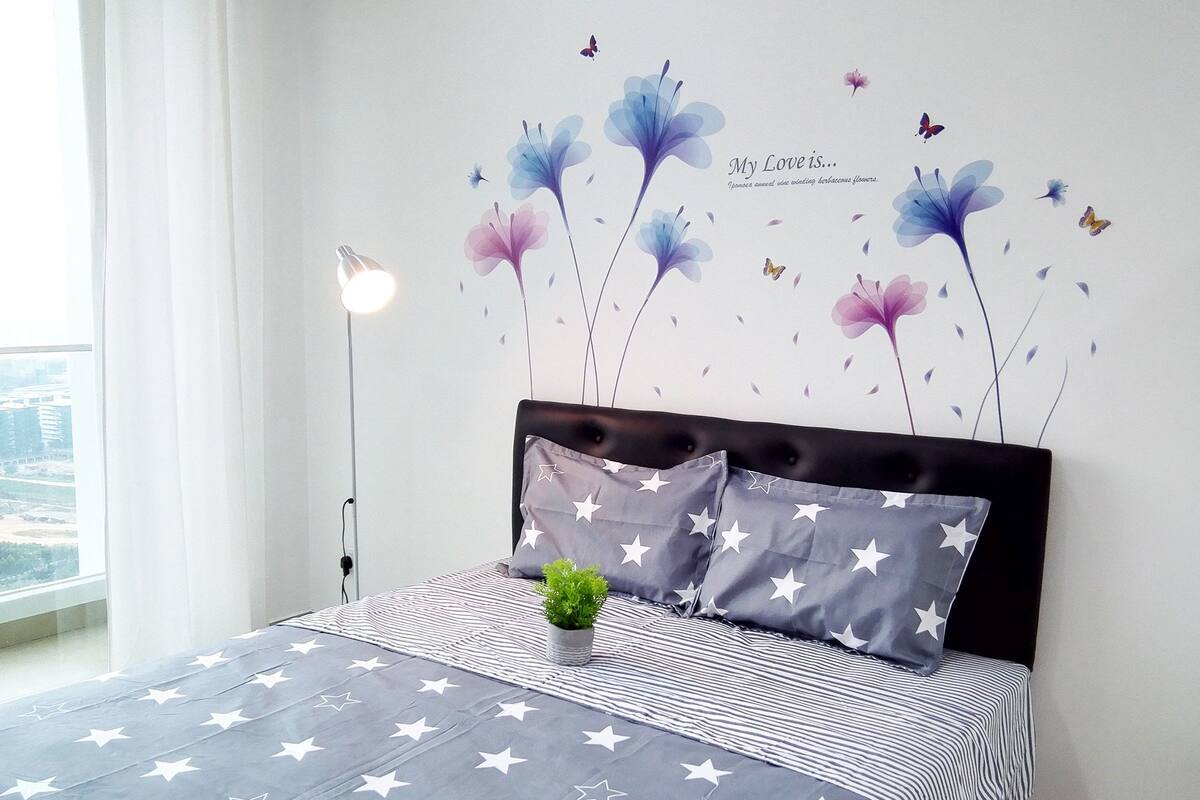 A bedroom with a bed, star-patterned bedding, a nightstand, a lamp, and a wall decoration of flowers and butterflies.