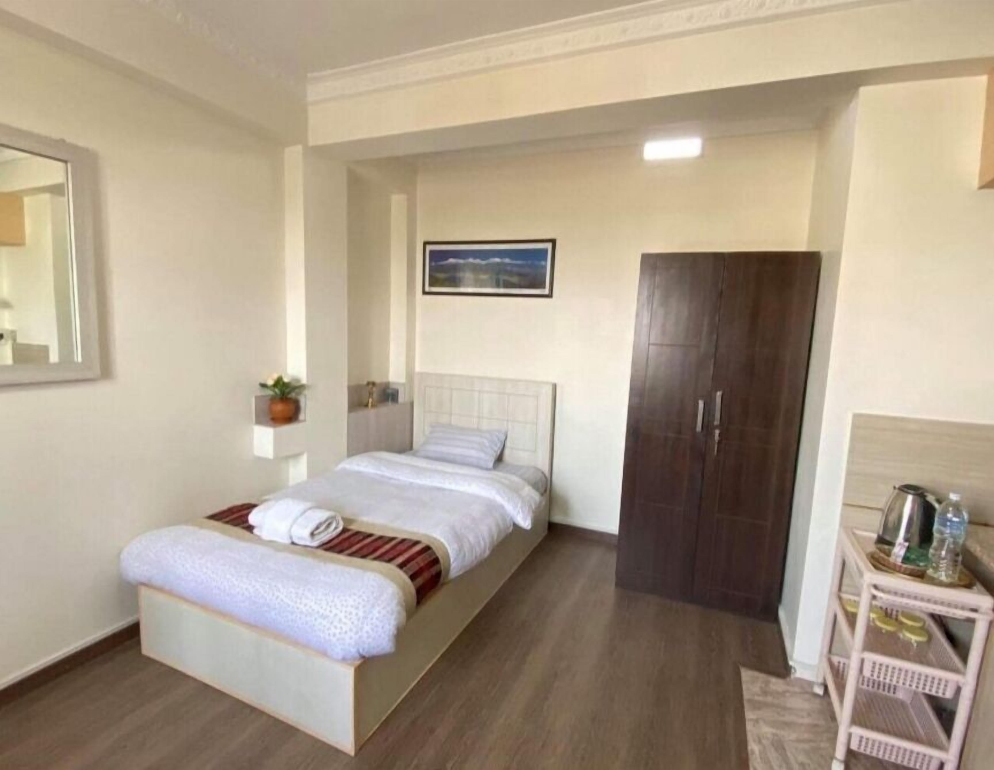 Ein Schlafzimmer mit Bett, Kleiderschrank, einem kleinen Tisch mit Wasserkocher und einem gerahmten Bild an der Wand.