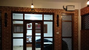 Una habitación con pared de ladrillo, puerta de madera con paneles de vidrio y un ventanal con celosía decorativa.
