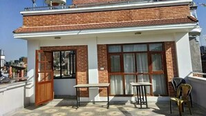 Un edificio de dos pisos con fachada de ladrillo, techo plano y un pequeño balcón con mesa y sillas.