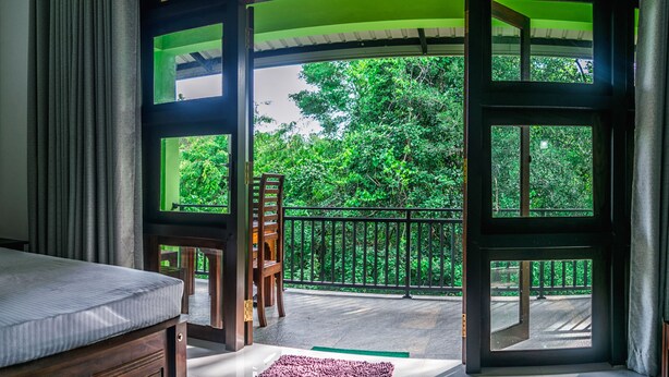 A room with a large window, a wooden chair, and a bed. - Wildescape Polonnaruwa (Polonnaruwa)