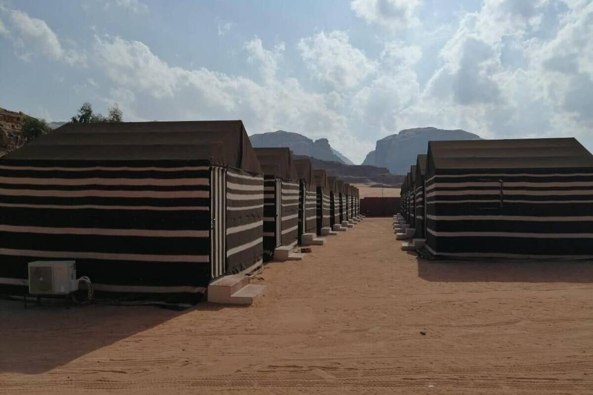 A row of striped tents in a desert setting with mountains in the background.