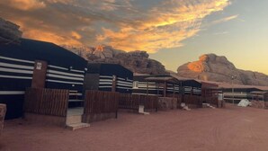 A desert landscape with a dirt road, wooden fences, and a building with striped awnings. - Sand Rose Camp - Hillawi Camp (Wadi Rum)