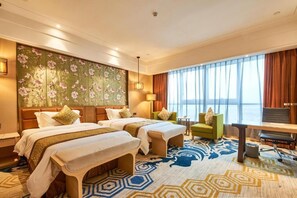 A hotel room with two beds, a desk, a chair, and a large window with curtains.