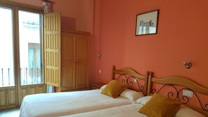 A room with two beds, a wooden wardrobe, a balcony with a view, and a framed picture on the wall. - Hotel San Miguel (Segovia)