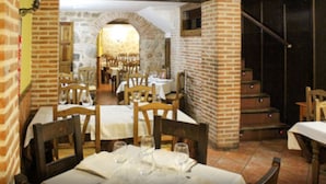 A restaurant with brick walls, wooden tables, and chairs. There are stairs leading to an upper level. - Hotel San Miguel (Segovia)