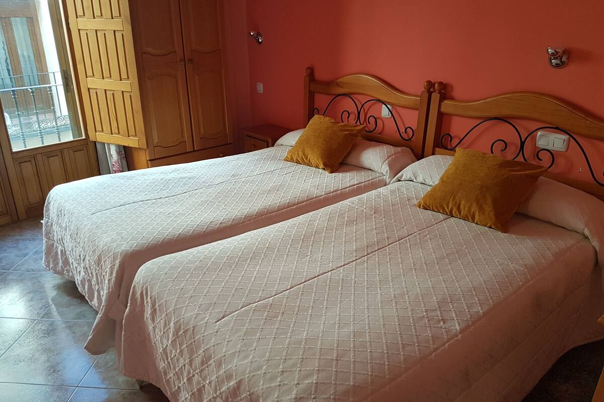 A room with two beds, wooden headboards, and a window with a view of a balcony.